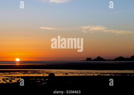 Le soleil se lève sur la mer à côté du phare et lifeboat cabanes dans Mumbles, Galles du Sud, jetant un brillant réflexion sur t Banque D'Images