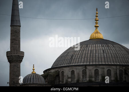 ISTANBUL, Turquie — les dômes en cascade de la mosquée du Sultan Ahmed, surmontés d'embouts dorés, s'élèvent contre un ciel nuageux. Le profil architectural distinctif de la mosquée comprend un dôme central entouré de quatre demi-dômes, créant la silhouette pyramidale caractéristique du bâtiment. Les flèches dorées au sommet de chaque dôme représentent des éléments architecturaux ottomans traditionnels. Banque D'Images