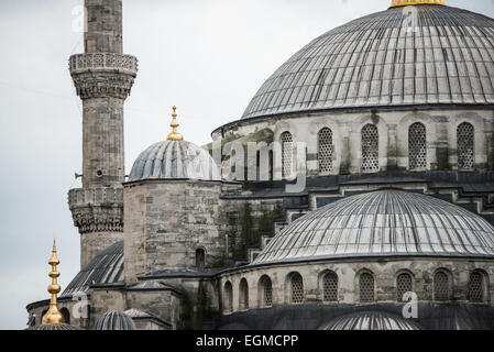 ISTANBUL, Turquie — les dômes en cascade de la mosquée du Sultan Ahmed, surmontés d'embouts dorés, s'élèvent contre un ciel nuageux. Le profil architectural distinctif de la mosquée comprend un dôme central entouré de quatre demi-dômes, créant la silhouette pyramidale caractéristique du bâtiment. Les flèches dorées au sommet de chaque dôme représentent des éléments architecturaux ottomans traditionnels. Banque D'Images