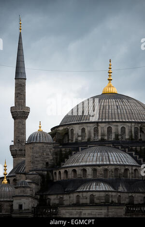 ISTANBUL, Turquie — les dômes en cascade de la mosquée du Sultan Ahmed, surmontés d'embouts dorés, s'élèvent contre un ciel nuageux. Le profil architectural distinctif de la mosquée comprend un dôme central entouré de quatre demi-dômes, créant la silhouette pyramidale caractéristique du bâtiment. Les flèches dorées au sommet de chaque dôme représentent des éléments architecturaux ottomans traditionnels. Banque D'Images