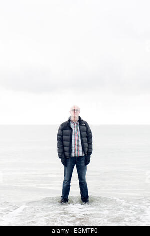 Man (dramaturge) Tim Crouch debout jusqu'aux chevilles dans la mer de se mouiller les pieds et chaussures à la recherche comme s'il marche sur l'eau Banque D'Images