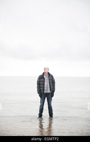 Man (dramaturge) Tim Crouch debout jusqu'aux chevilles dans la mer de se mouiller les pieds et chaussures à la recherche comme s'il marche sur l'eau Banque D'Images