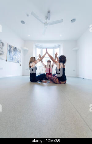 Trois femmes de participer à un groupe de remise en forme yoga class, dans une salle vide. L'idée est que vous demandez à vos partenaires Banque D'Images