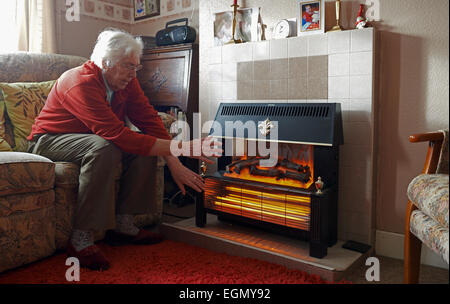 Ancien pensionné au chaud à la maison à côté d'un feu électrique Banque D'Images