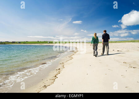 Jeune femme et homme marchant le long d'une belle plage de sable dans le soleil d'été, Burray, îles Orcades, en Écosse. Banque D'Images