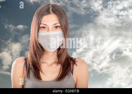 Chinese woman wearing surgical mask avec ciel nuageux en arrière-plan Banque D'Images