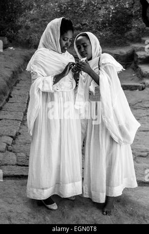 Deux femmes pèlerins vêtus de vêtements blancs traditionnels regarder des photos sur un téléphone mobile, Bete Maryam Church, Lalibela Banque D'Images