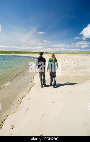 Jeune femme et homme marchant le long d'une belle plage de sable dans le soleil d'été, Burray, îles Orcades, en Écosse. Banque D'Images