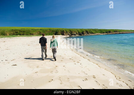 Jeune femme et homme marchant le long d'une belle plage de sable dans le soleil d'été, Burray, îles Orcades, en Écosse. Banque D'Images