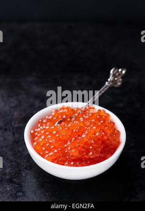 Caviar de saumon dans un bol blanc sur fond sombre, selective focus Banque D'Images
