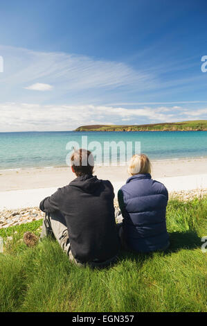 Jeune couple assis à côté d'une belle plage de sable, South Ronaldsay, îles Orcades, en Écosse. Banque D'Images