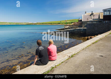 Jeune femme et l'homme se détendre au bord de la mer à St Margaret's Hope, îles Orcades, en Écosse. Banque D'Images