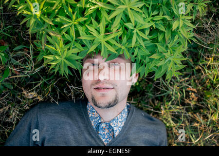 Portrait d'un jeune homme allongé sur le sol avec des feuilles o la tête Banque D'Images