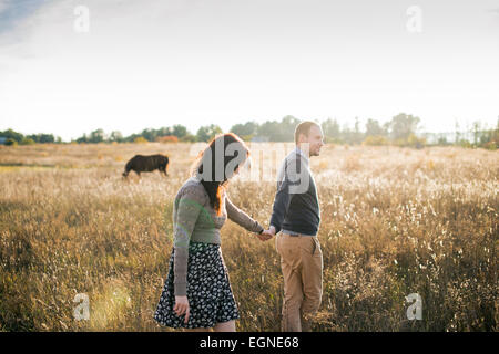 Image d'un jeune couple qui marche main dans la main au coucher du soleil d'automne. Chevaux sur l'arrière-plan. Banque D'Images