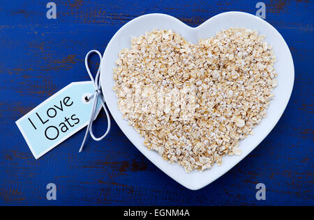 Assiette d'aliments nutritifs et sains des flocons d'avoine dans un bol en forme de coeur bleu foncé sur table en bois rustique, avec J'aime l'avoine variable de message. Banque D'Images