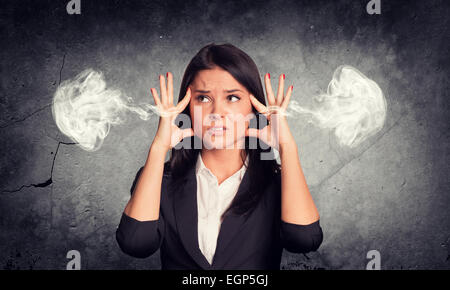 Frustrated woman holding doigt pour son temple, la fumée des oreilles. Mur de béton en arrière-plan Banque D'Images