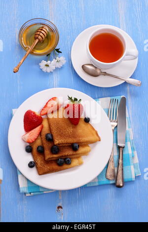 Pile de crêpes aux bleuets, fraises fraîches, miel, thé, vue du dessus Banque D'Images