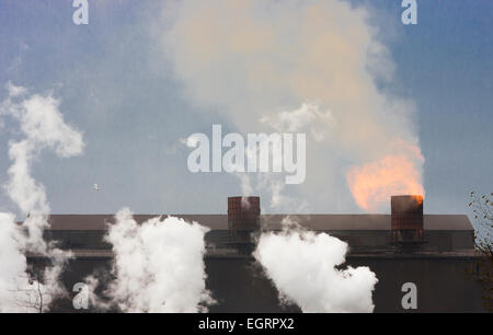 La pollution industrielle et les flammes de coulage de cheminées sur le toit de l'usine d'acier sale crasseux avec Brume de chaleur et de fumée les nuages de vapeur Banque D'Images