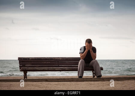 Homme triste est assis sur le vieux banc en bois sur la côte. Tons Vintage Retro photo avec effet de filtre de tonalité Banque D'Images