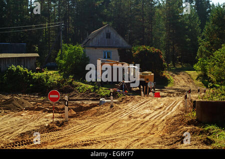 La construction de routes.Le constructeur sur l'excavatrice creuse le sable pour le pont - un tuyau à travers un flux. Banque D'Images