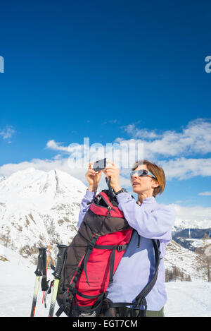 Sac à dos alpinisme femmes avec la prise de photo avec smart phone dans la main pour le majestueux panorama des Alpes italiennes en mer d'hiver Banque D'Images