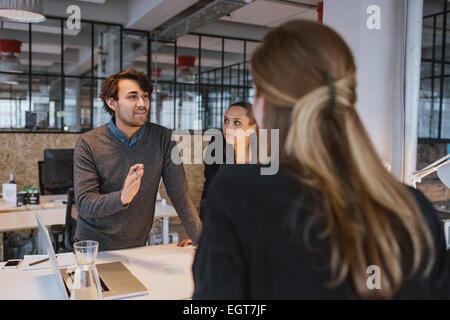 Jeune homme expliquant nouveau plan d'affaires à des collègues au cours d'une réunion autour d'une table dans Office. Banque D'Images