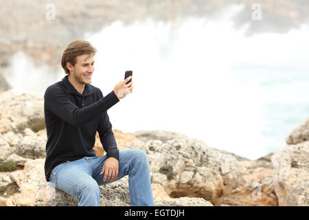 L'homme en utilisant un téléphone intelligent en hiver sur la plage avec l'océan en arrière-plan Banque D'Images