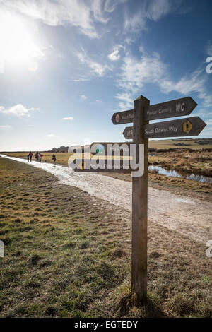 Day trippers font leur chemin vers la plage de Cuckmere Haven ona beau jour d'hiver suivant les instructions du sol en bois Banque D'Images