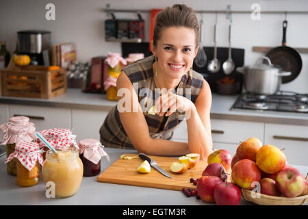 Jeune femme au foyer, debout près de pots de confiture et fruits eating apple Banque D'Images