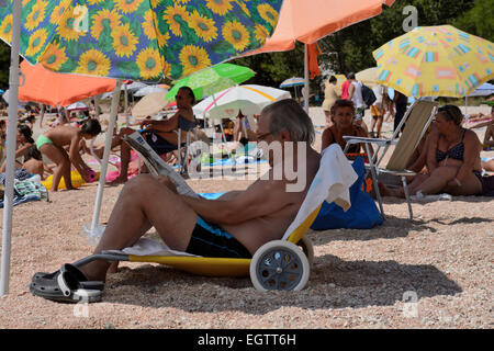 Touriste italien en Sardaigne s'assit sur la plage lire le journal Banque D'Images