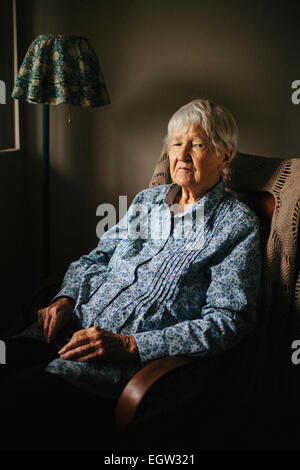 Senior woman in blue shirt sitting in chair. Banque D'Images