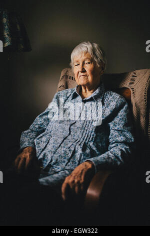 Senior woman in blue shirt sitting in chair. Banque D'Images