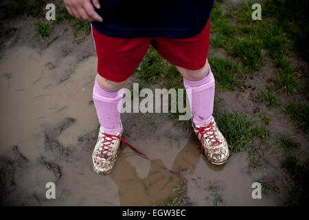 Girl joue au soccer dans le champ boueux. Banque D'Images