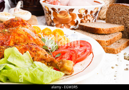 Cuisses de poulet rôti avec des tranches de tomates Salade complète herbes sur nappe blanche, vue du dessus Banque D'Images