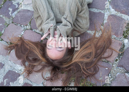 Cute young girl lying on la chaussée de pierre avec des cheveux. Banque D'Images