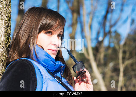 Pretty woman posing in the woods en hiver holding sunglasses Banque D'Images
