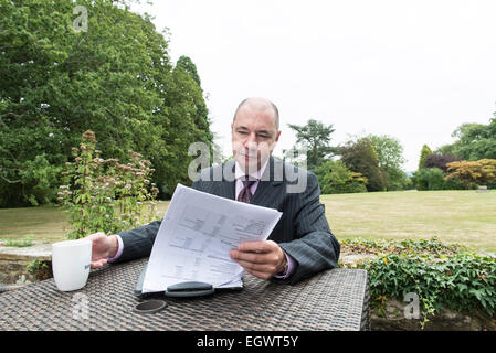 Une ambiance d'affaires professionnel / manager est assis à une table de travail à l'extérieur avec une tasse de café dans un costume sur une belle journée Banque D'Images