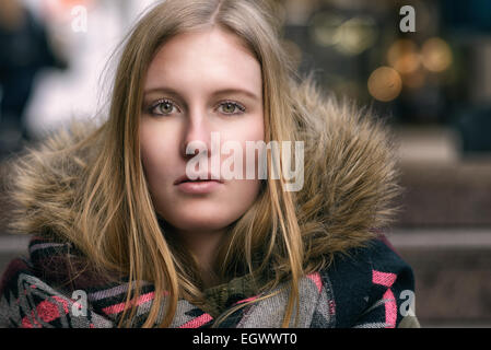 Jolie jeune femme blonde grave vêtu d'une fourrure chaude veste d'hiver à directement à l'appareil photo, Close up tête et sho Banque D'Images