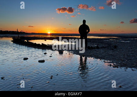 Whitstable, Kent, UK. 3 mars 2015 : Météo France. Un homme regarde un glorieux coucher de soleil sur une ancienne péniche coup sur Whitstable front de mer à marée basse après une journée avec une touche de printemps dans l'air malgré un vent frisquet Banque D'Images