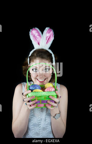 Jeune femme posant avec oreilles de lapin et oeufs de Pâques Panier avec sur fond noir. Banque D'Images