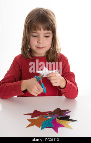 Petite fille jouant avec des étoiles en papier avec des paillettes de couleurs Banque D'Images