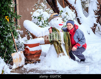 Femme est posant avec un bonhomme dans sa cour pendant une tempête de neige Banque D'Images