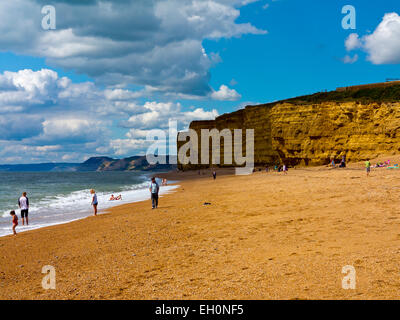 Les gens qui jouent sur la plage avec des falaises de grès derrière à Burton Bradstock sur la côte jurassique du sud-ouest de l'Angleterre UK Banque D'Images