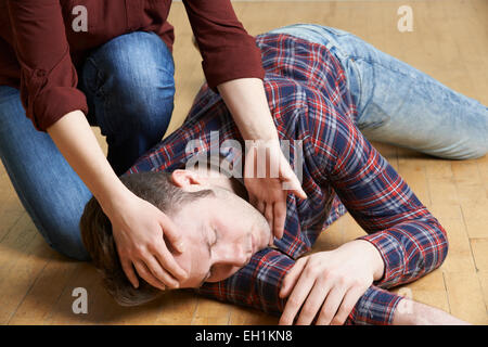 Femme de placer l'homme dans la position de récupération après accident Banque D'Images