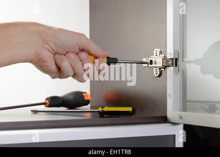 Un homme utilise un tournevis pour régler une charnière dissimulée fixé sur un cabinet moderne avec une porte en verre Banque D'Images