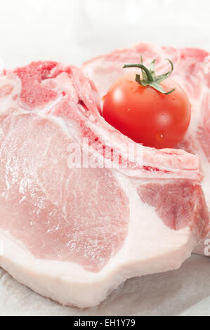 Côtelettes de porc tacheté de matières premières et d'une tomate à l'alimentation papier. Banque D'Images