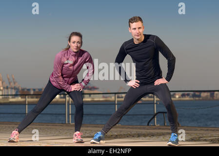 Jeune couple exerçant au bord de l'article sur l'esplanade en face du port réchauffe leurs muscles stretching Banque D'Images