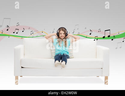 Smiling little girl in headphones sitting on sofa Banque D'Images