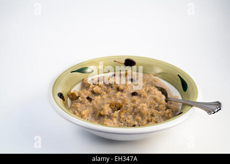 Bol de gruau sains et nutritifs avec les raisins secs dans un bol en grès sur un fond blanc Banque D'Images