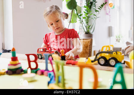 3 ans, fille, dans une robe rouge joue avec des jouets pour son anniversaire à la table, Allemagne Banque D'Images